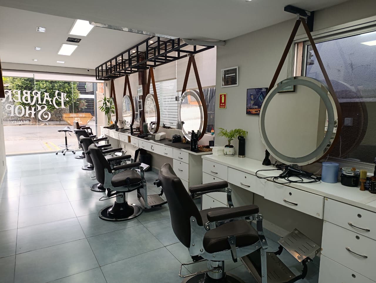 Ambiente da barbearia, com cadeiras de couro e espelhos redondos
