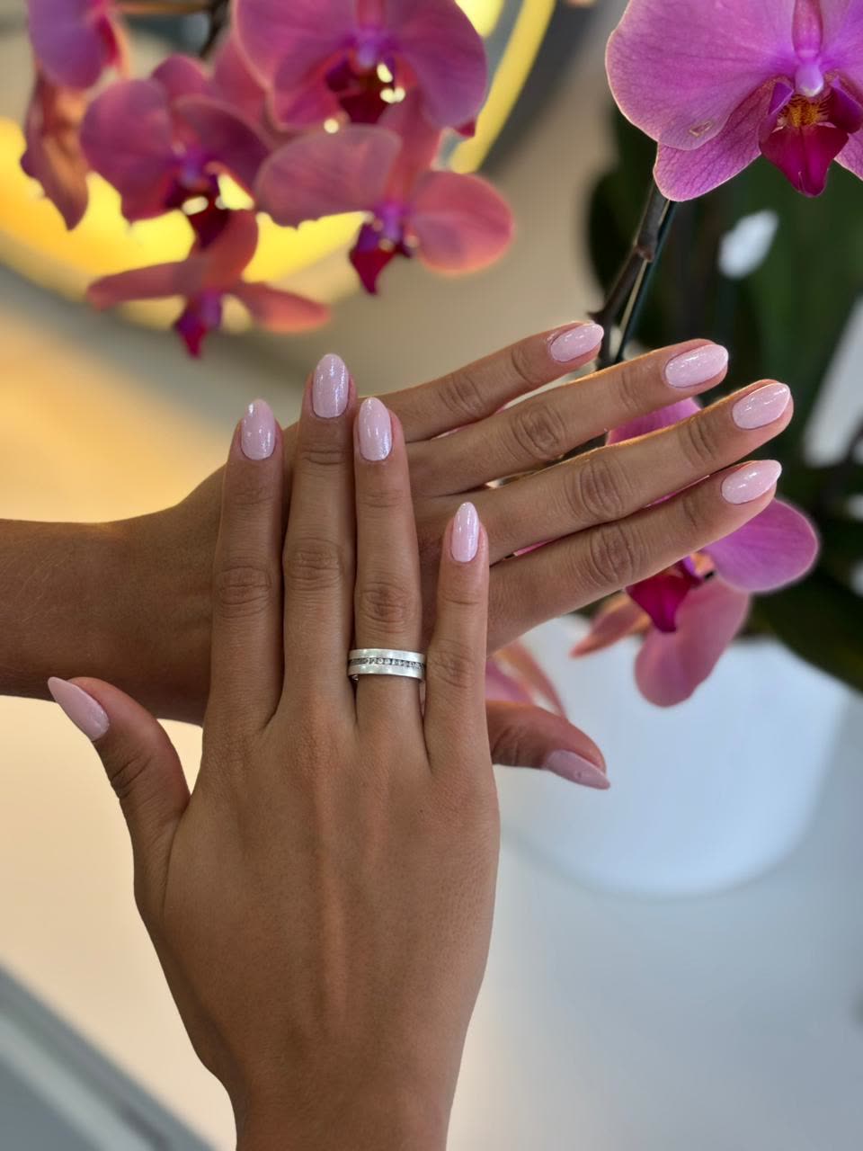 Unhas em tom claro com orquídeas ao fundo